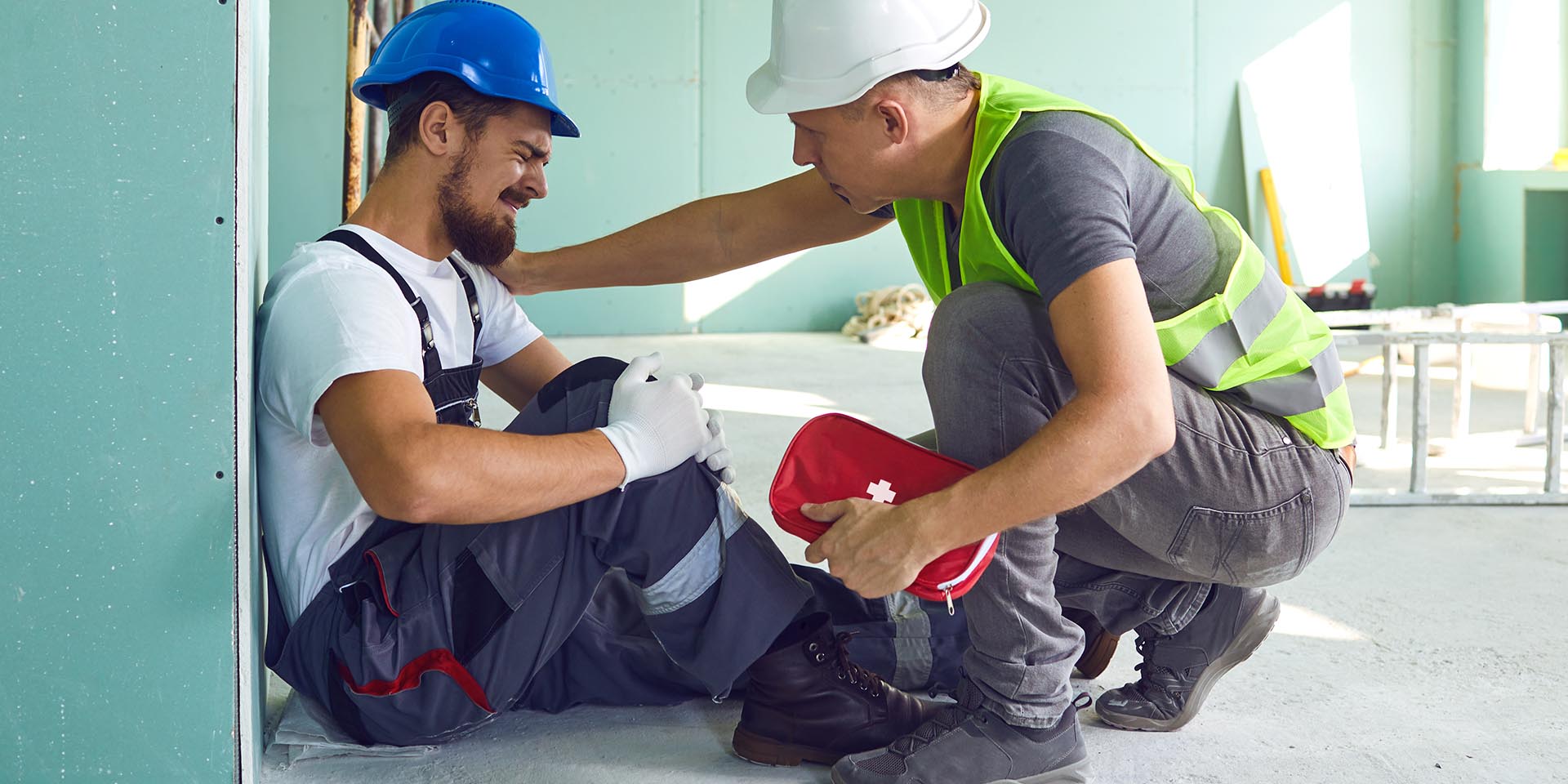 Ein Mitarbeiter erleidet einen Arbeitsunfall während ein anderer Mitarbeiter mit einem Erste-Hilfe-Kit aushilft. © Adobe Stock, Studio Romantic