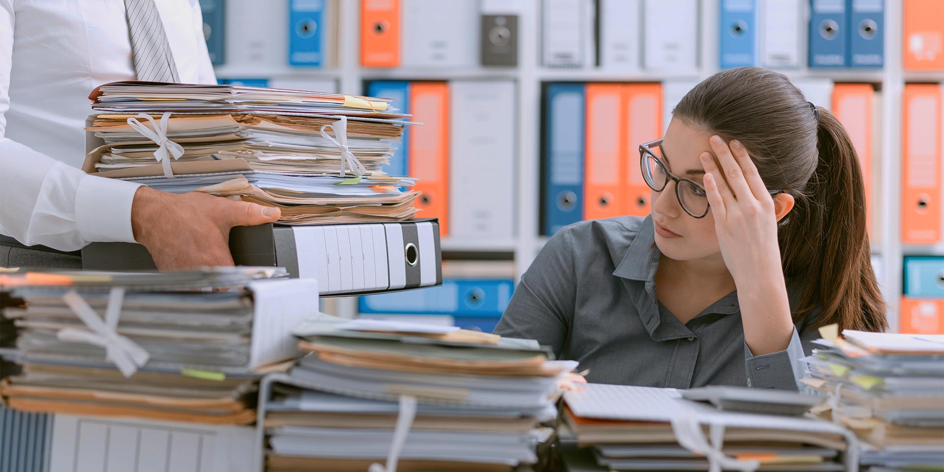Eine Mitarbeiterin ist von der Dokumenten- und Ordneranzahl im Büro überfordert. © Adobe Stock, StockPhotoPro