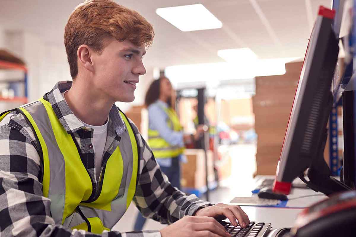 Azubi in gelber Sicherheitsweste arbeitet selbstständig an einem PC im Lagerraum. © Adobe Stock, Monkey Business