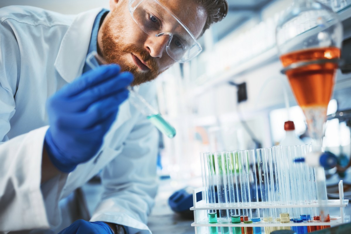 Ein Mitarbeiter in einem Chemie-Labor überprüft flüssige Chemikalien in Reagenzgläsern. © Adobe Stock, NDABCREATIVITY