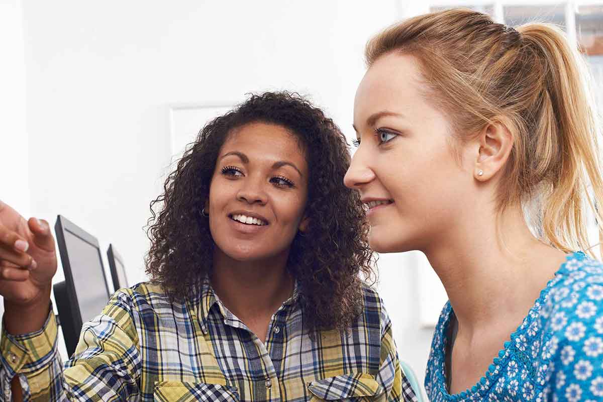 Mitarbeiterin arbeitet mit einer Auszubildenden zusammen am PC und erklärt ihr wesentliche Zusammenhänge. © Adobe Stock, highwaystarz