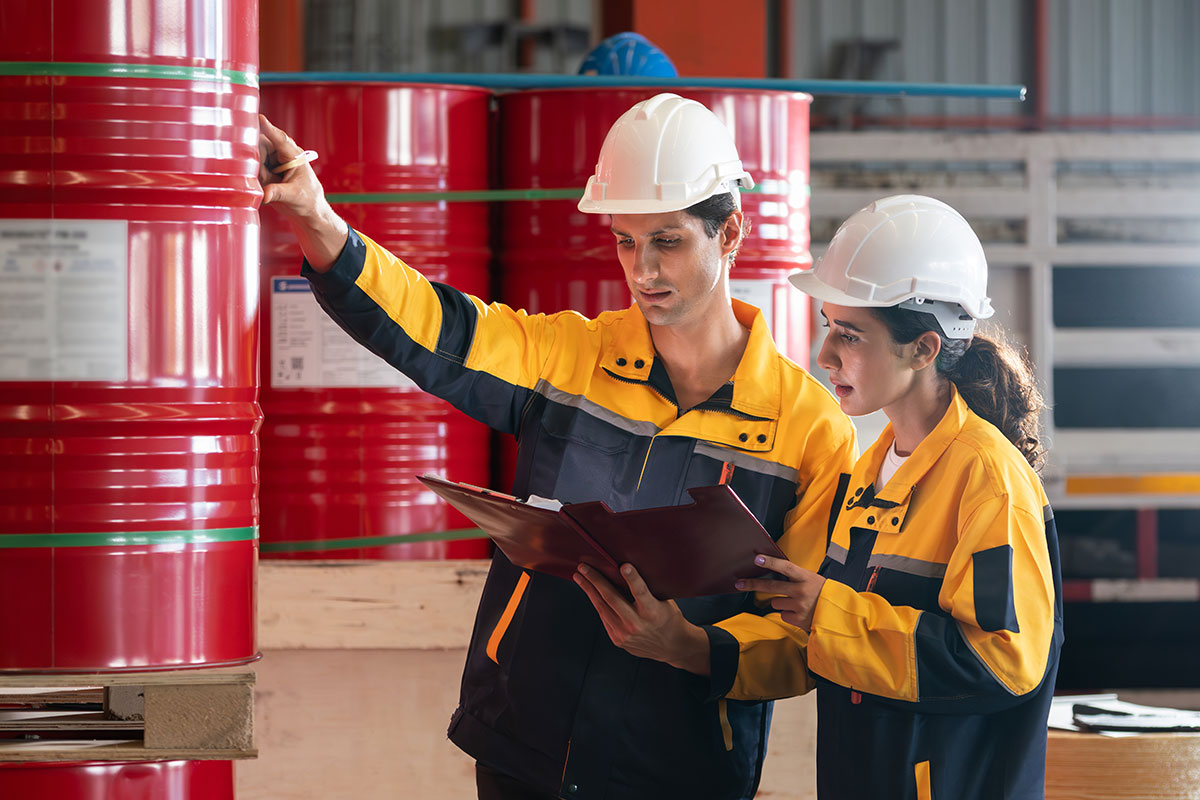 Mitarbeiter in Schutzausrüstung erfassen die Lagerung von Gefahrstoffen auf ihrem Klemmbrett.
