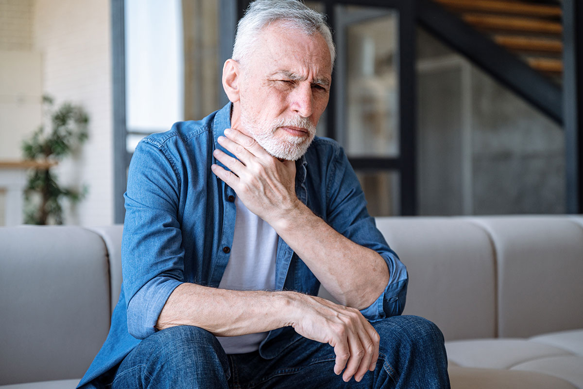 Ein älterer Mann reibt sich krank die Kehle – er leidet unter Spätfolgen durch den früheren beruflichen Umgang mit Gefahrstoffen.