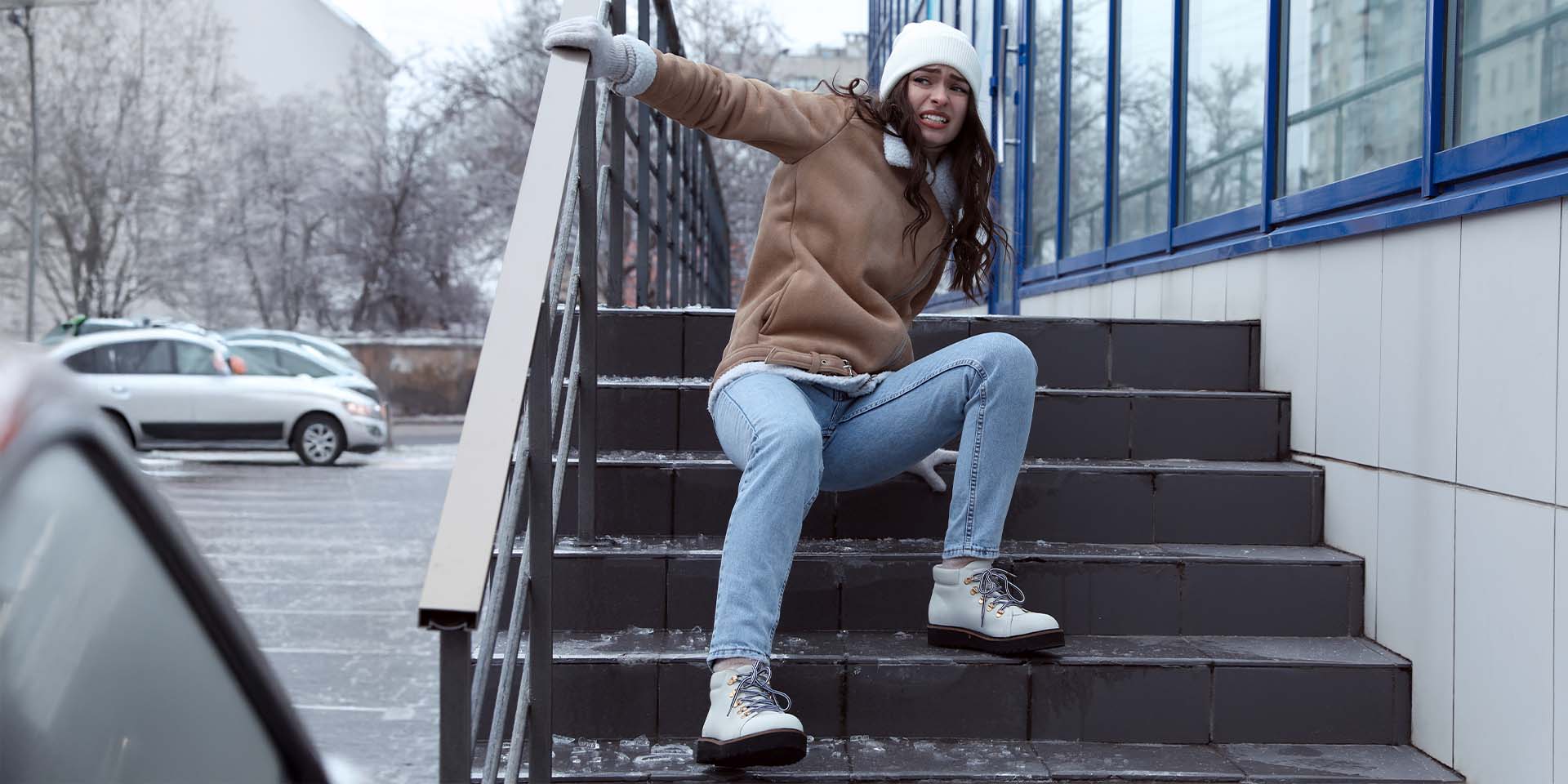 Eine Frau rutscht auf einer glatten Treppe am Gebäude im Winter aus.